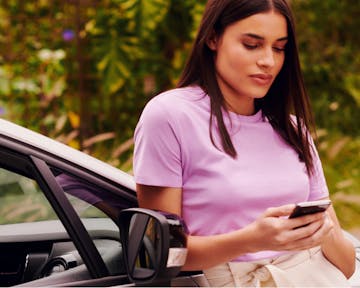 mulher encostada em um carro olhando para a tela do celular