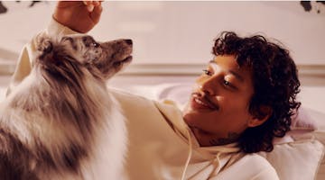 man laying in bed smiling while playing with his dog