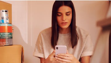 Woman sitting on the floor with cell phone in hands looking at investment options to apply her money.