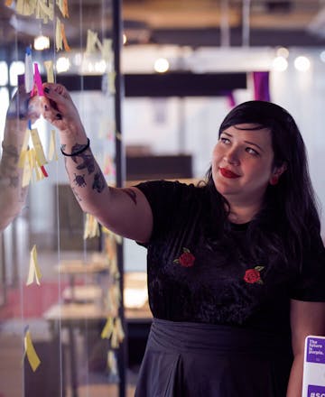 Image of a woman in the Nubank office sticking a post-it note on a glass wall.