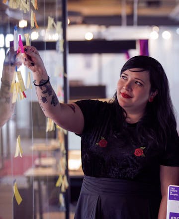 Image de uma mulher no escritório do Nubank colando um post-it em uma parede de vidro.