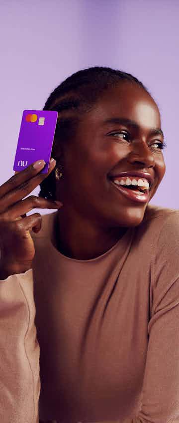 Imagem de uma mulher sorrindo enquanto segura o cartão do Nubank próximo ao rosto.