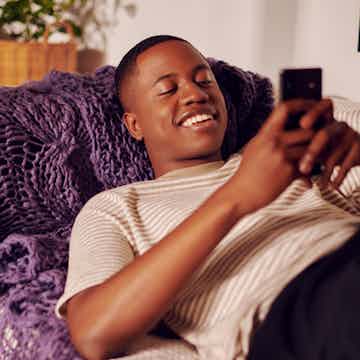 imagem de um homem sorrindo deitado no sofá enquanto usa o celular