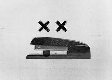 Grampeador com dois X nos olhos e uma língua caída em preto e branco e aparência de impressão antiga em fax.