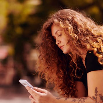 mulher de cabelos ruivos cacheados vista de perfil enquanto mexe no celular