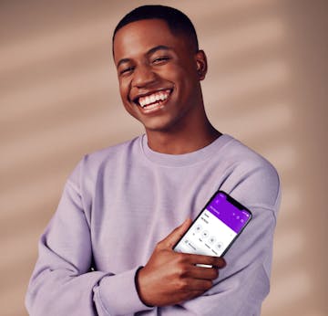 Homem preto, com cabelos raspados, vestindo um moletom roxo e segurando um celular com o aplicativo do Nubank aberto.