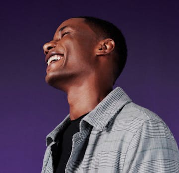 Homem preto sorrindo com fundo roxo