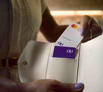 Foto de uma mulher segurando uma carteira com um cartão PF do Nubank e inserindo o cartão PJ do Nubank.