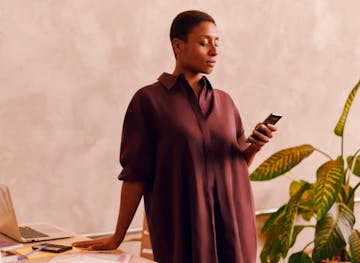 Woman with black skin, short curly hair, wearing a long brown shirt. She's standing there fiddling with his cell phone.