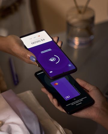 pessoa segurando uma máquina de cartão, enquanto a outra efetua o pagamento pelo celular através da tecnologia contactless pelo app Nubank