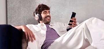 homem ouvindo música no sofá enquanto olha para o celular