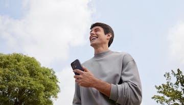 Mulher sentada no chão com o celular em mãos olhando as opções de investimentos para aplicar seu dinheiro.