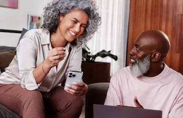 Woman with cell phone and man with laptop in living room