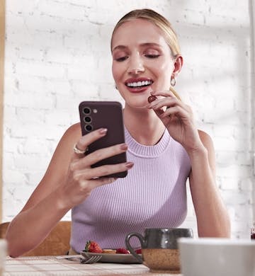 Woman looking at cell phone and eating fruit at a table