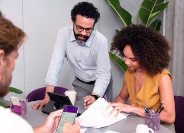 Homem verificando app Nubank no escritório com dois colegas.