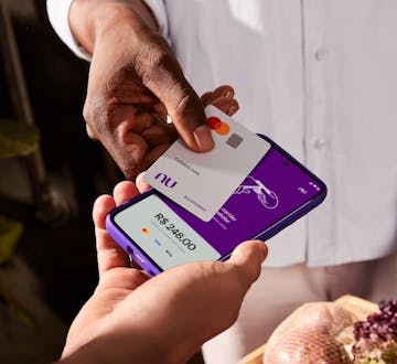 Uma mão segurando um celular enquanto outra aproxima um cartão cinza do nubank